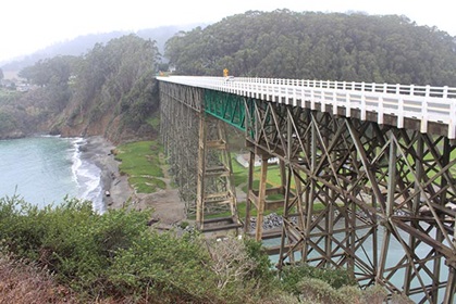 A massive arch bridge connecting one hillside to another, over an inlet.
