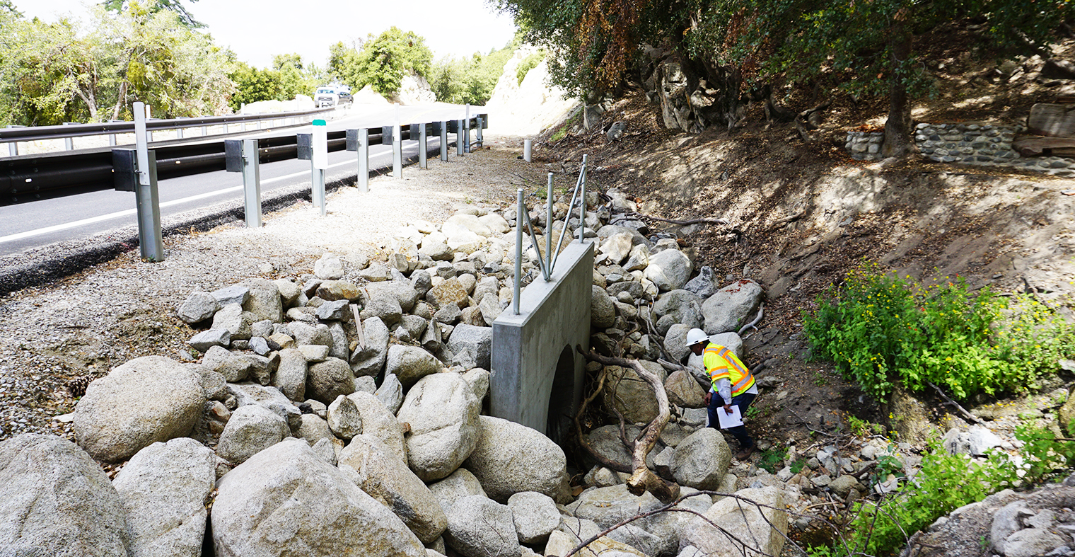 Photo of a Caltrans inspector looking over a newly installed culvert.